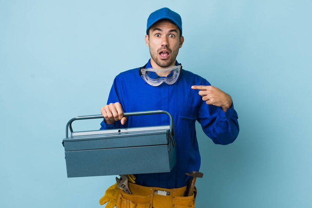 young adult hispanic man looking shocked and surprised with mouth wide open, pointing to self. toolbox concept and plumber - Fotoğraf, Görsel