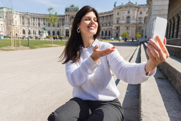 happy woman taking selfie on smartphone while gesturing in vienna  - Φωτογραφία, εικόνα