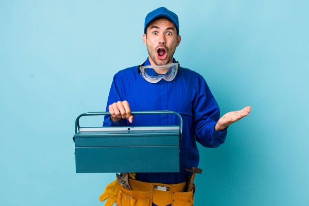 young adult hispanic man feeling extremely shocked and surprised. toolbox concept and plumber - Foto, imagen