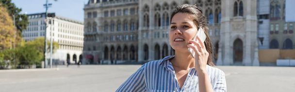 ウィーンの路上で携帯電話で話している縞模様のシャツを着た陽気な女性バナー - 写真・画像