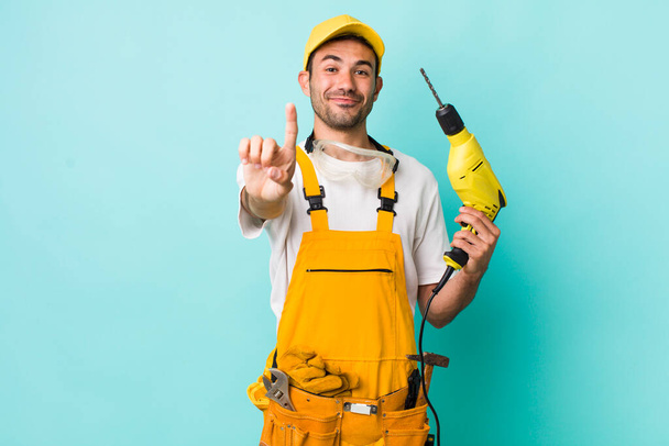 young adult hispanic man smiling proudly and confidently making number one. worker and drill concept - Photo, Image