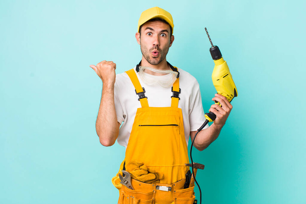 young adult hispanic man looking astonished in disbelief. worker and drill concept - 写真・画像