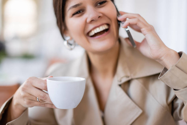 щаслива жінка тримає чашку і розмовляє на смартфоні на літній терасі
  - Фото, зображення