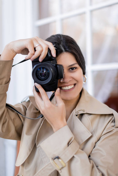 happy photographer in trench coat taking photo on digital camera  - 写真・画像