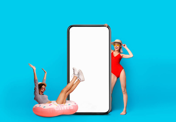 Two Cheerful Excited Multiethnic Women Wearing Summer Outfits Posing Near Blank Smartphone - Foto, Imagem