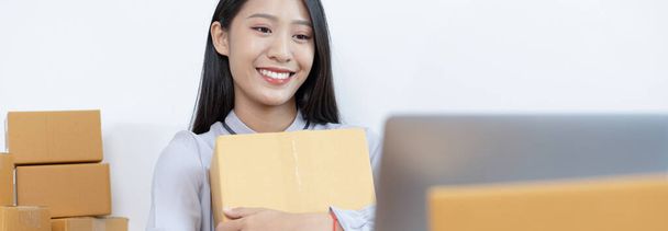 Young Asian woman chatting with a customer on a laptop and displays the product before delivery to confirm the order, Selling products online or doing freelance work at home concept. - Foto, Imagen