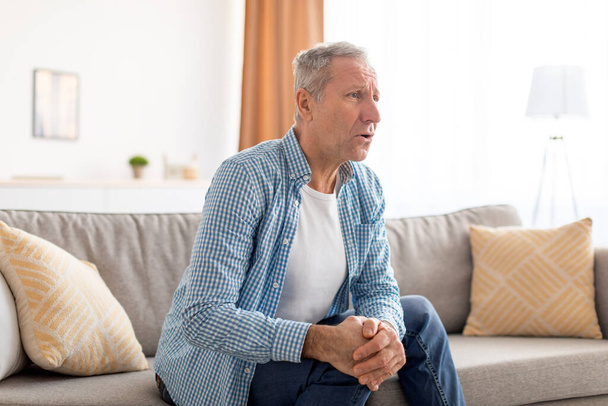 Starší muž s bolestí kolena sedí doma na gauči - Fotografie, Obrázek
