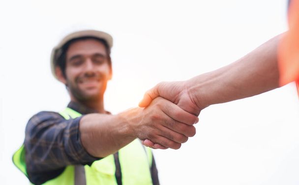 Handsome construction engineer in protective helmets and vests are shaking hands while working in the office center - Photo, Image