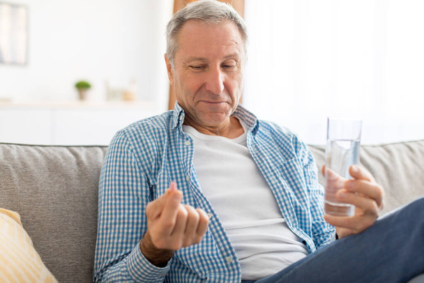 Felnőtt férfi tablettákat szed egy pohár vizet tartva. - Fotó, kép