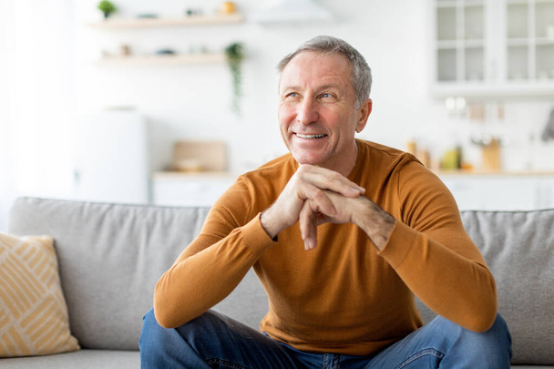 Smiling mature man sitting on the couch and thinking - Foto, Imagem