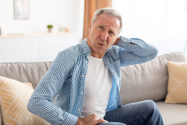 Nemocný dospělý muž sedí na gauči, masíruje krk - Fotografie, Obrázek