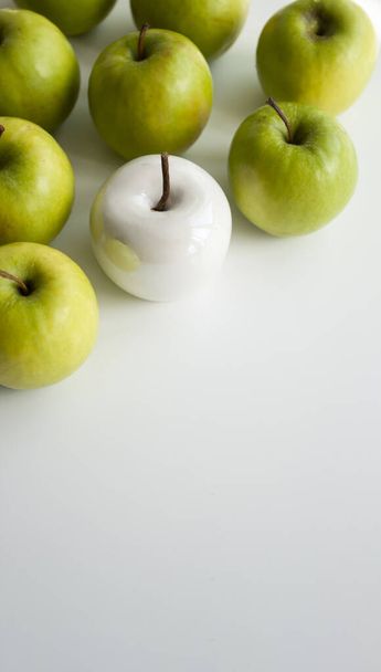 Багато яскраво-зелених яблук і одна біла кераміка лежать на білому однорідному тлі. Концептуальне фото
. - Фото, зображення