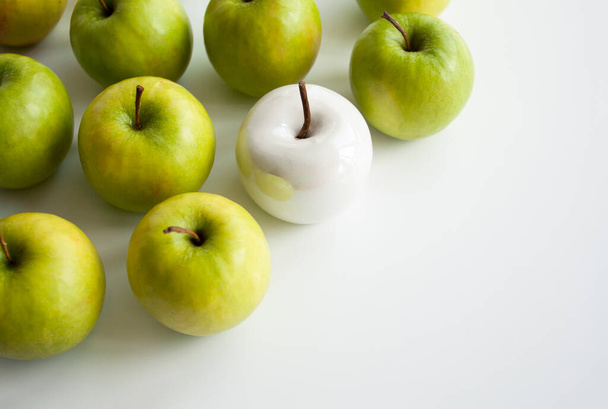 Many bright green apples and one white ceramic lie on a white uniform background. Conceptual photo. - Фото, изображение