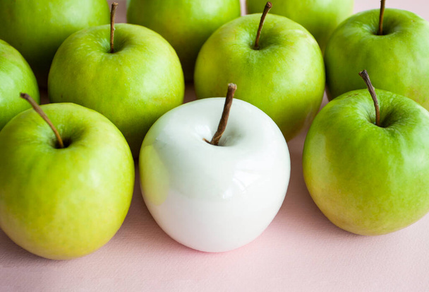 Many bright green apples and one white ceramic lie on a pink uniform background. Conceptual photo. - Foto, Imagen