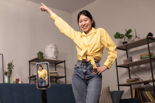 Cheerful Asian woman dancing at camera filming video on cellphone - Foto, Bild