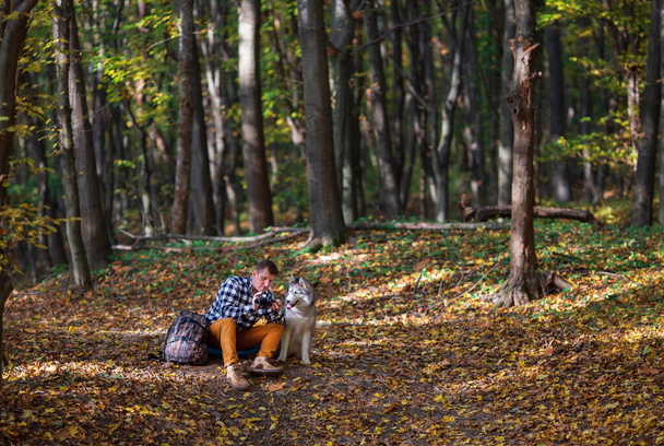Jonge man die met zijn Siberische husky hond midden in het herfstbos loopt. Concept van menselijke en dierlijke vriendschap - Foto, afbeelding