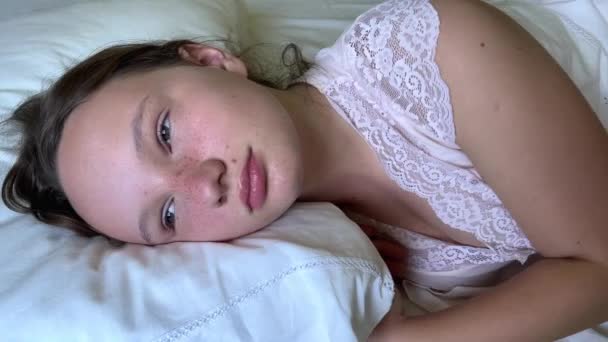 een meisje met sproeten ligt op een wit bed ze opent haar ogen ze werd net wakker en glimlacht - Video