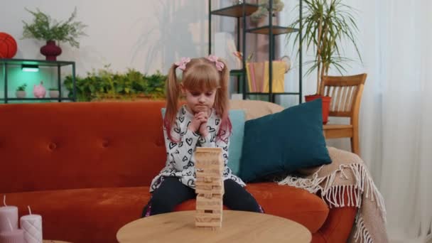 Küçük, komik bir kız çocuğu modern oturma odasında tahta bloklar tuğla oyunu oynuyor. - Video, Çekim
