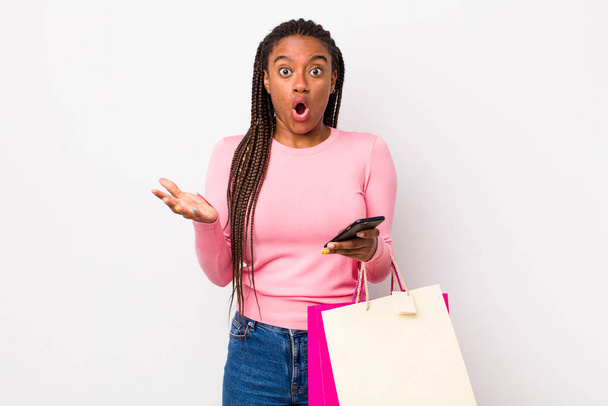 young adult black woman feeling extremely shocked and surprised. shopping bags concept - Fotó, kép