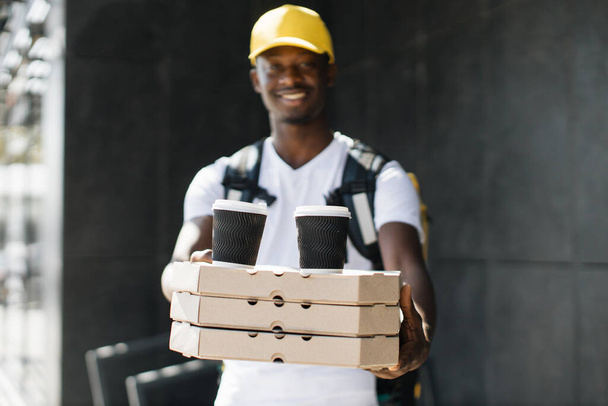 Young happy african delivery man with yellow thermal box backpack and cap. - Foto, Bild