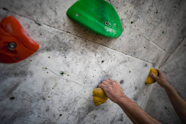 Close-up tiro de uma mão masculina manchado com pó de magnésio agarrando um porão de uma parede de escalada, no ginásio. - Foto, Imagem