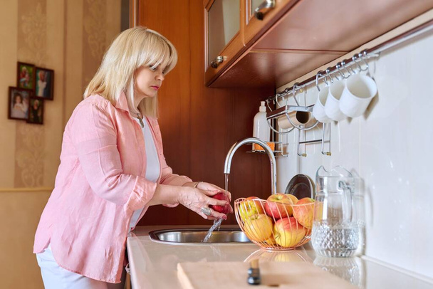 Mature woman washing apples at home in the kitchen - Foto, imagen