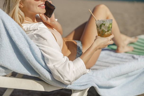 Cropped shot of lady on deck chair, having call and cocktail on a sunny day - Photo, Image