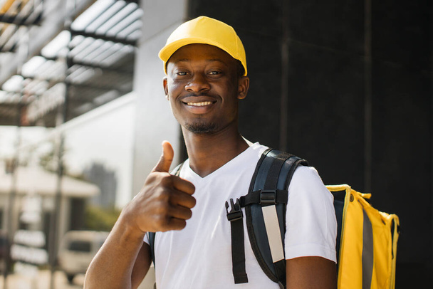 Food delivery, portrait of courier african man with yellow backpack and cap. - Φωτογραφία, εικόνα