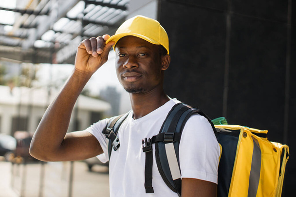 Portrait of delivery man with yellow cap and thermal backpack looking at camera. - Foto, Bild
