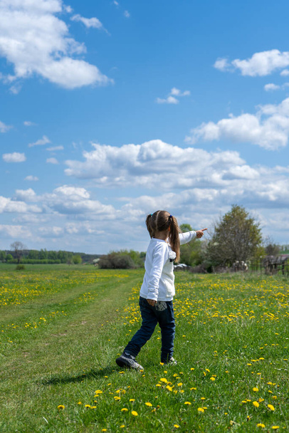 Little girl walks in a beautiful spring field and shows her hand forward. Adventure and exploring concept. High quality photo - Photo, Image