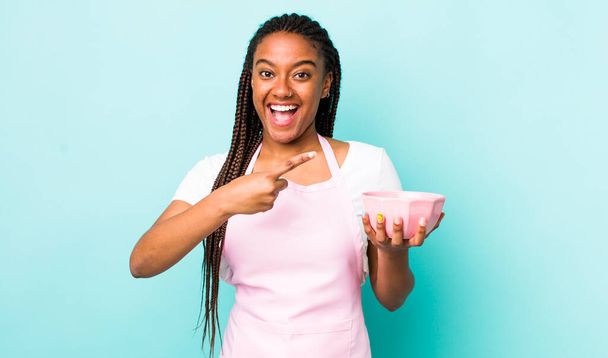 young adult black woman looking excited and surprised pointing to the side. empty bowl concept - Foto, Imagem