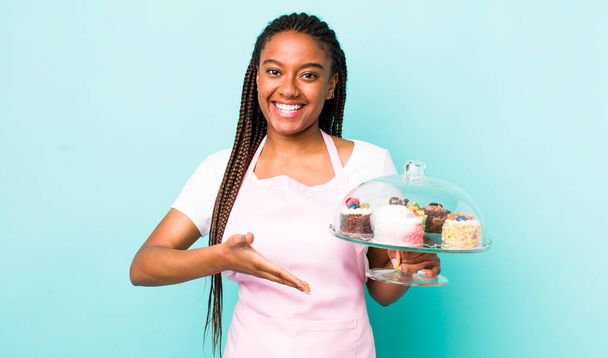 young adult black woman smiling cheerfully, feeling happy and showing a concept. home made cakes concept - Fotoğraf, Görsel