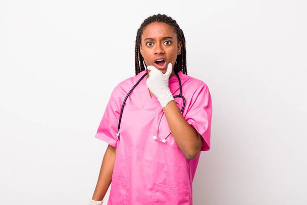 young adult black woman with mouth and eyes wide open and hand on chin. veterinarian concept - Foto, Bild