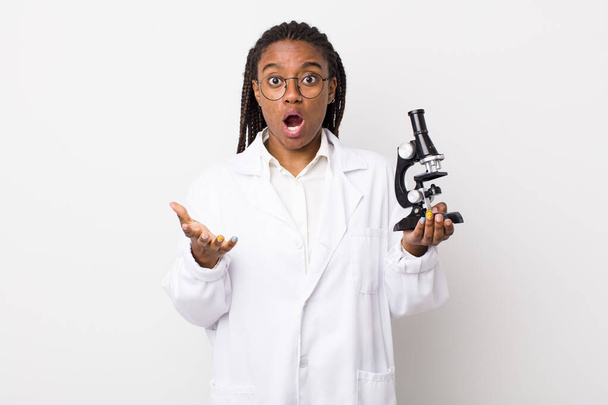 young adult black woman feeling extremely shocked and surprised. sciencist with microscope - Foto, Bild