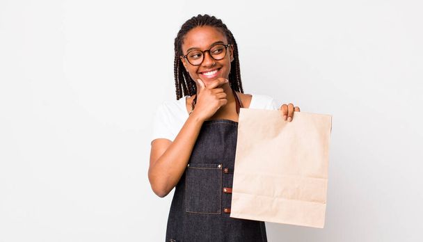 young adult black woman smiling with a happy, confident expression with hand on chin. take away delivery concept - Foto, immagini