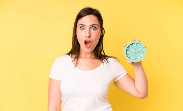 young adult pretty woman looking very shocked or surprised. alarm clock concept - Φωτογραφία, εικόνα