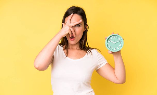 young adult pretty woman looking shocked, scared or terrified, covering face with hand. alarm clock concept - Foto, Bild