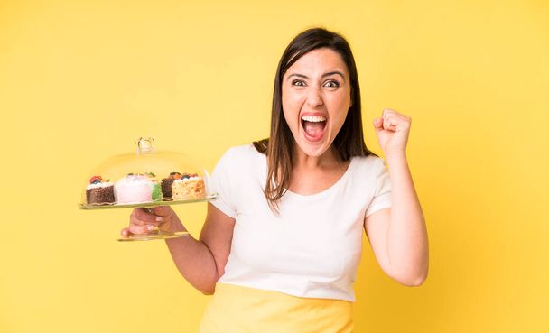 young adult pretty woman shouting aggressively with an angry expression. homemade cakes concept - 写真・画像