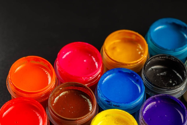 close-up background of opened small gouache paint jars on black surface - Fotó, kép