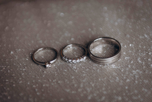 The wedding rings of the bride and groom in white gold lie on a shiny white veil. Wedding. Engagement. - Fotoğraf, Görsel