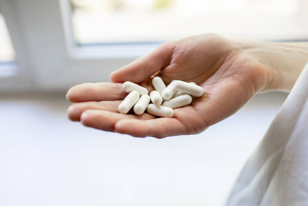 Ręka człowieka z białymi tabletkami w dłoni. Medyczna koncepcja leczenia chorób lekami. Witaminy na każdy dzień. Dużo tabletek w ręku z antybiotykami. - Zdjęcie, obraz
