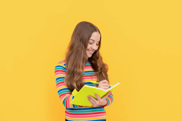 Happy girl dziecko zapisać w copybook żółty tle, umiejętności czytania i pisania - Zdjęcie, obraz