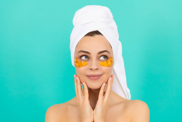 χαμογελαστή νεαρή γυναίκα έχει κολλαγόνο επιθέματα χρυσό μάτι στο πρόσωπο με πετσέτα - Φωτογραφία, εικόνα