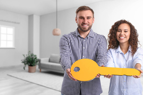Ευτυχισμένο νεαρό ζευγάρι με μεγάλο χάρτινο κλειδί στο νέο τους σπίτι. - Φωτογραφία, εικόνα