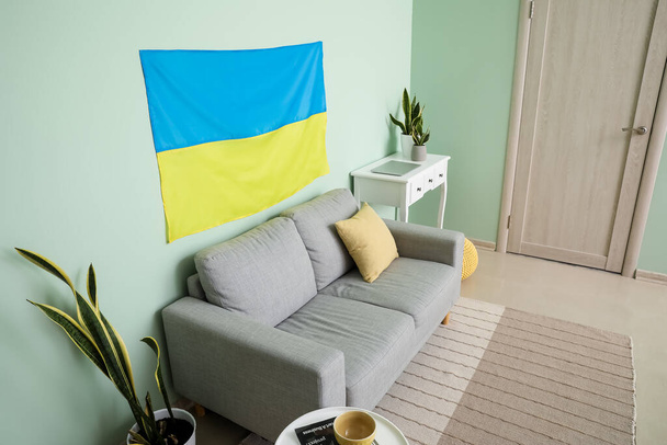 Interno del soggiorno con comodo divano e bandiera dell'Ucraina appeso sulla parete a colori - Foto, immagini