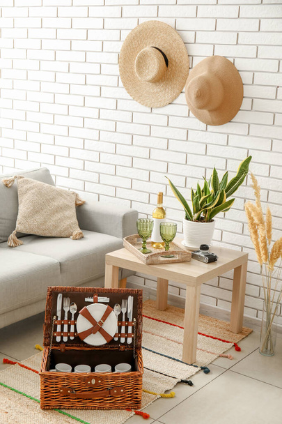 Wicker basket with tableware for picnic on carpet in living room - Photo, Image