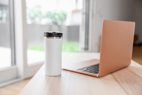 Laptop and thermos on coffee table in room, closeup - Foto, Bild