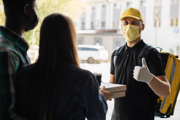 Smilling delivery man in yellow face mask, uniform cap delivering cardboard boxes with pizza - Valokuva, kuva