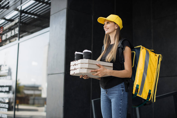 Courier delivering boxes with pizza and hot coffee. Young girl delivering food to customers - Foto, afbeelding