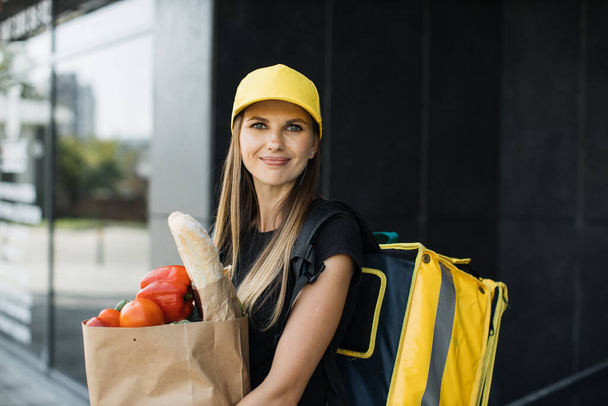 Smiling delivery woman holding paper bag with organic vegetables. - Φωτογραφία, εικόνα
